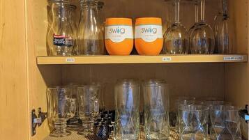 A kitchen with shelves holding various glassware, including shot glasses, wine glasses, and a colander.