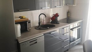 Une cuisine moderne avec des meubles gris, un évier en acier inoxydable, une bouilloire rouge et un four à micro-ondes.