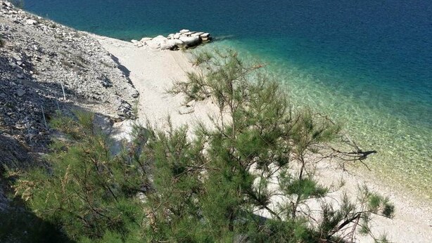 Une plage côtière bordée d’une eau turquoise et limpide, de sable blanc et d’un paysage rocheux.