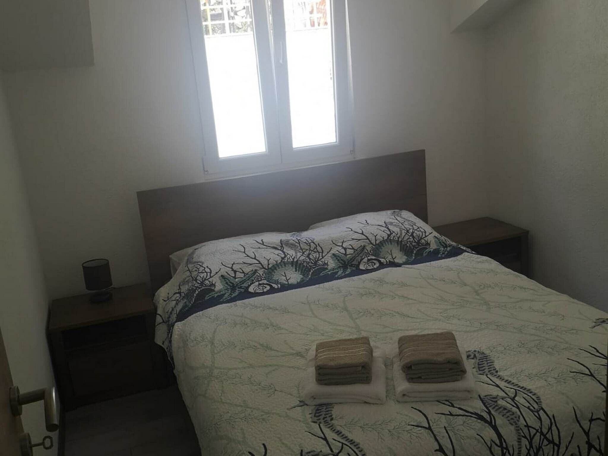 A bedroom with a bed, a nightstand, a lamp, and a window.