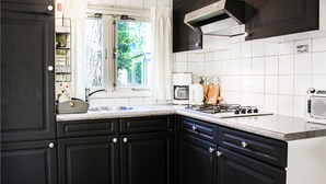 Una cocina con armarios oscuros, una encimera blanca, una estufa a gas, una cafetera y un ventanal con cortinas.