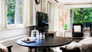 Una sala de estar moderna con una mesa redonda, un televisor y vistas al exterior con vegetación.