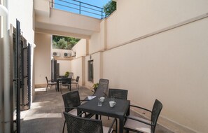 Een klein terras buiten met een tafel en stoelen, airconditioners aan de muur en uitzicht op groen.
