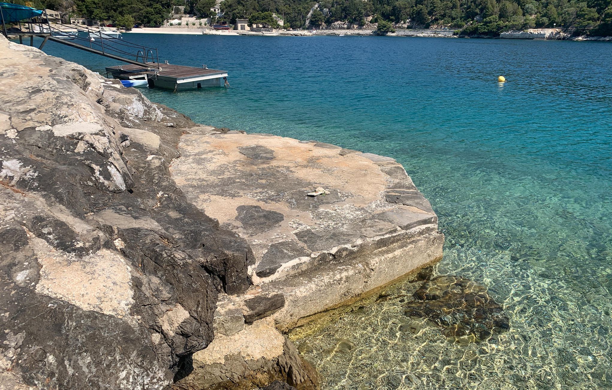 Eine felsige Küste mit klarem Wasser, einer Anlegestelle und Booten.