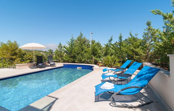 A swimming pool with blue tiles, surrounded by lounge chairs and a covered umbrella. - Gorgeous apartment in Selca with house sea view (Selca)