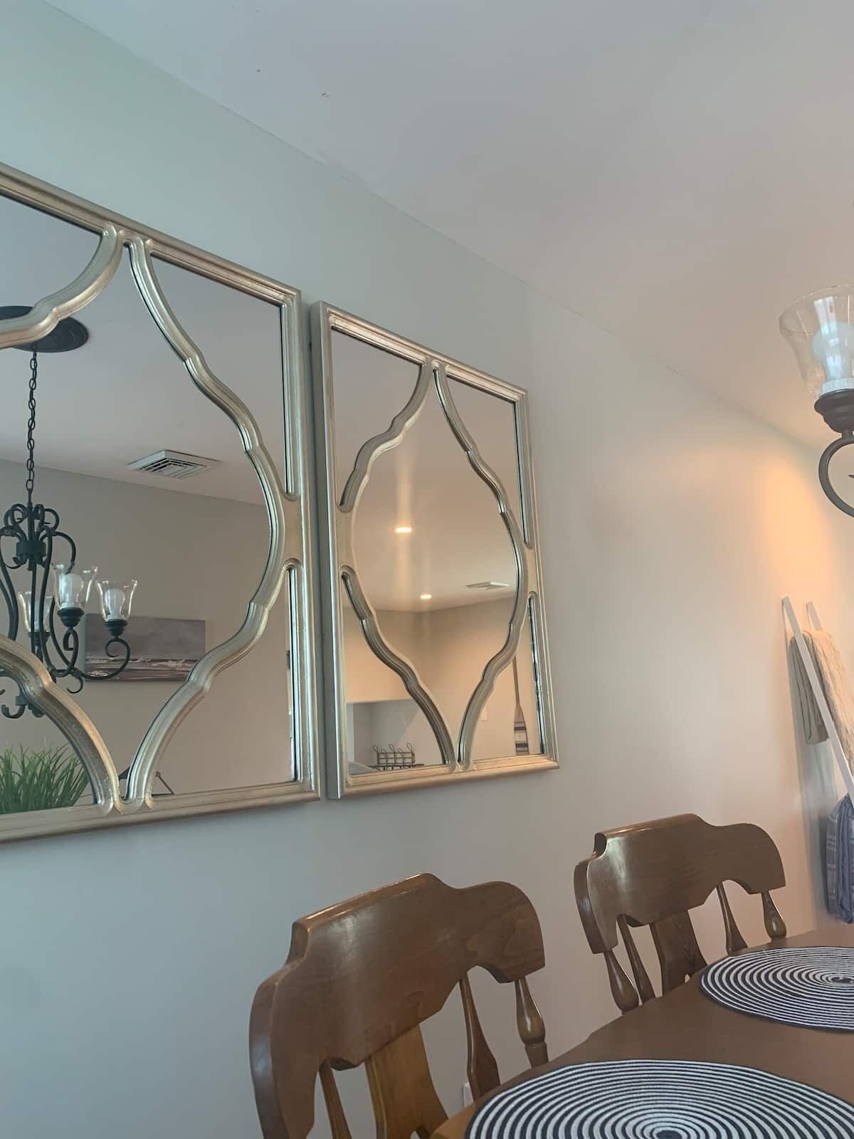 Un espace repas comprenant une table, des chaises et deux miroirs fixés au mur.
