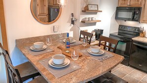 Une cuisine dotée d’un plan de travail en granit, une table à manger mise avec des assiettes, des bols et des verres à vin, un panneau indiquant l’emplacement du coin café, et un four à micro-ondes.