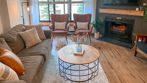 Un salon comprenant un canapé, deux fauteuils, une table basse, une cheminée et un téléviseur.