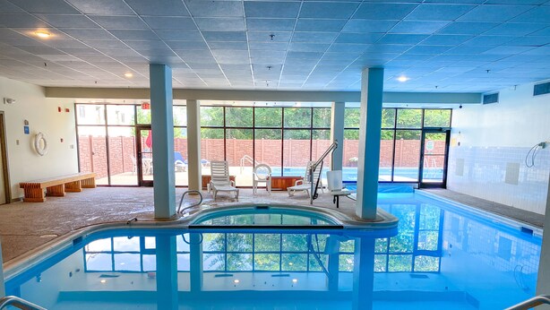 Une piscine intérieure offrant une vue dégagée sur l’extérieur, entourée de grandes fenêtres et agrémentée de quelques chaises longues.