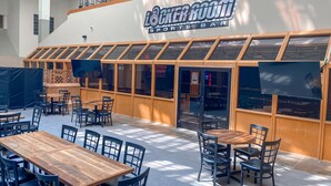 Un bar sportif intérieur doté de nombreuses tables et chaises en bois, de grandes fenêtres et d’un plafond haut.