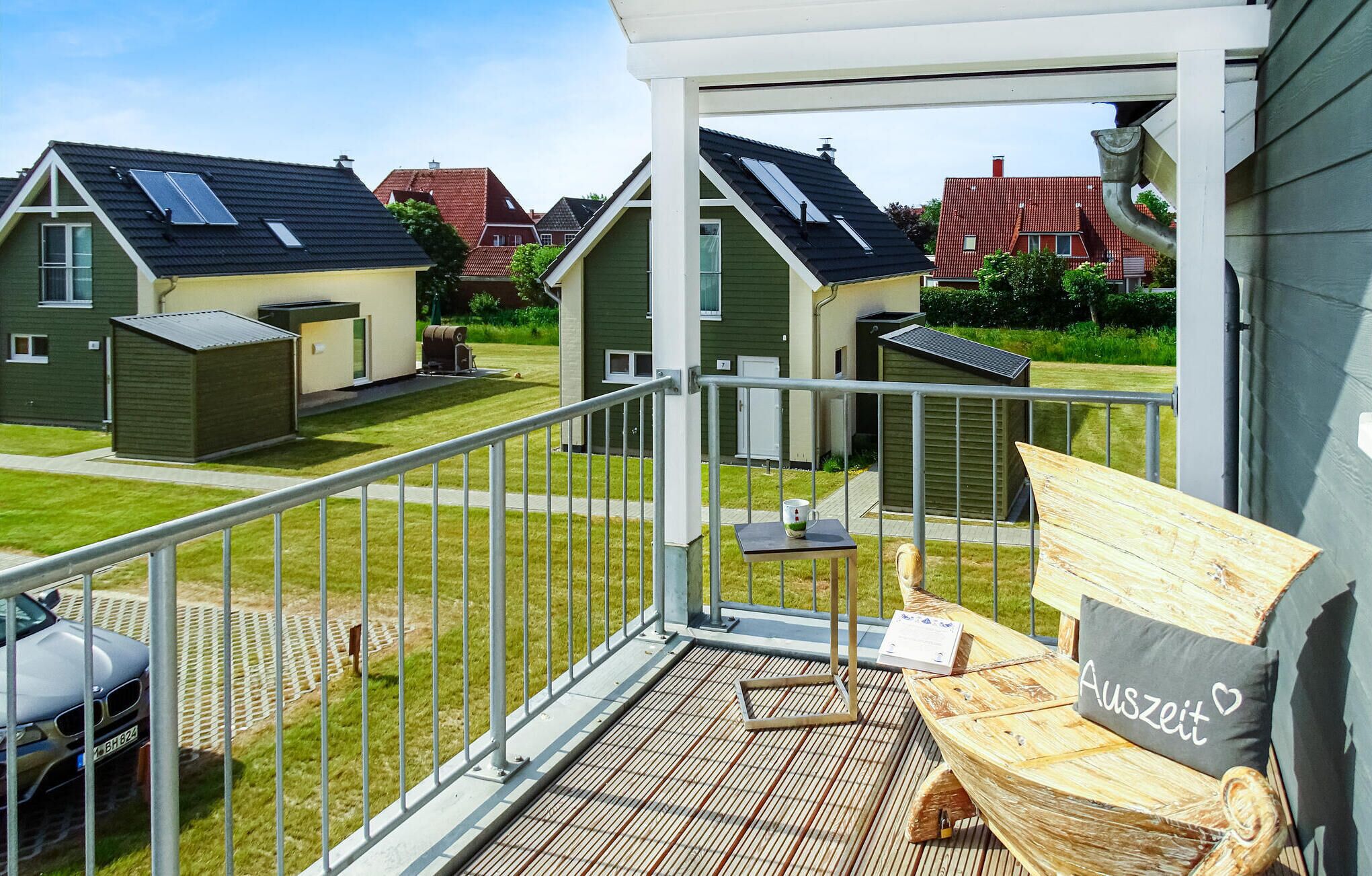 A balcony with a metal railing, a wooden bench, and a cushion with the word "Auszeit" on it.