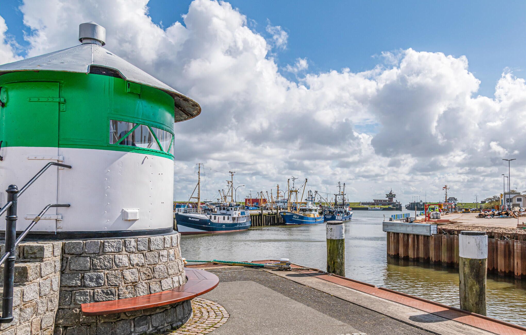 A harbor with boats docked, a lighthouse, and a stone wall.