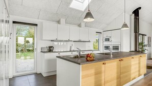 Eine moderne Küche mit weißen Schränken, einer zentralen Kochinsel mit Holzvertäfelung, Edelstahlgeräten und einem Oberlicht.