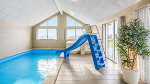 Ein Hallenbad mit einer blauen Rutsche, einer Leiter und einer großen Kübelpflanze.