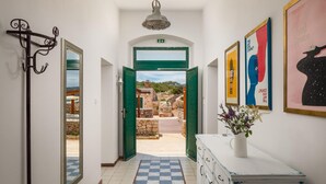Un couloir avec un sol à carreaux, un porte-manteau, une porte verte donnant sur l’extérieur et une commode blanche sur laquelle est posé un vase de fleurs.