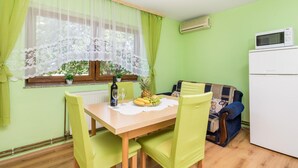 A small dining area with a table set for two, a window with lace curtains, a microwave, and a refrigerator.