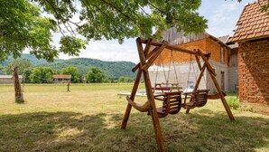 A wooden swing set in a grassy yard with a brick building in the background.