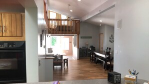 Une cuisine moderne dotée d’un four encastré, un coin repas avec une longue table et un espace en mezzanine agrémenté d’un ventilateur de plafond.