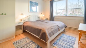 Ett sovrum med en säng, sängbord, ett litet bord, ett fönster med gardiner, ett element och en tavla på väggen.