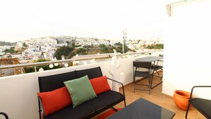 A balcony with a black sofa, a table, and chairs, overlooking a cityscape.