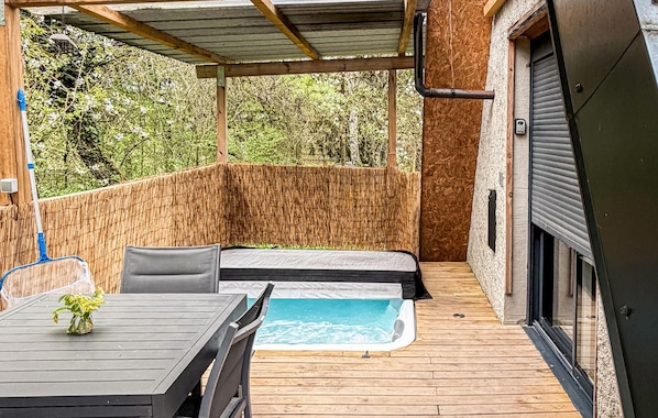 Un patio techado con jacuzzi, terraza de madera y una mesa con sillas.