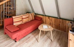 Un sofá rojo con almohadones a rayas, una pequeña mesa de madera con un libro, y suelo de madera.