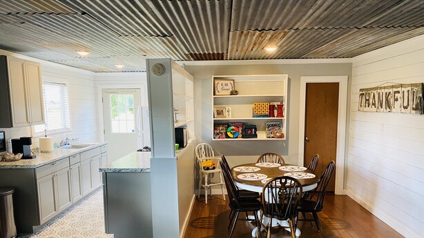 Una cocina moderna con una isla central, una zona de comedor con una mesa redonda y sillas, y un espacio de estar con una estantería y objetos decorativos.