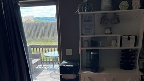 A room with a sliding glass door leading to a patio, a kitchenette with a coffee maker, and a shelf with decorative items. - Beautiful! (Black Hawk)