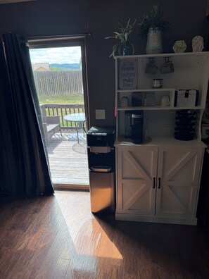 A room with a sliding glass door leading to a patio, a kitchenette with a coffee maker, and a shelf with decorative items.
