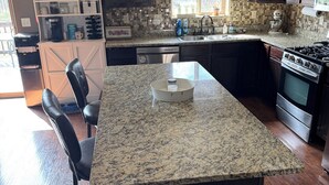 A kitchen with a granite island, dark cabinets, a dishwasher, a stove, and a window with blinds. - Beautiful! (Black Hawk)