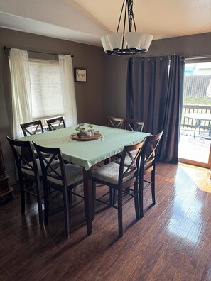 A dining area with a table set for four, wooden chairs, a chandelier, and a view of the outdoors.