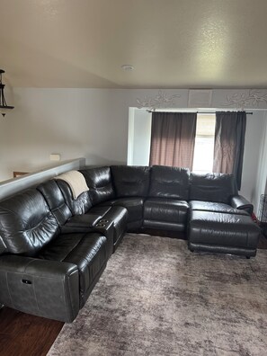 A living room with a sectional sofa, a fireplace, and a window with curtains.
