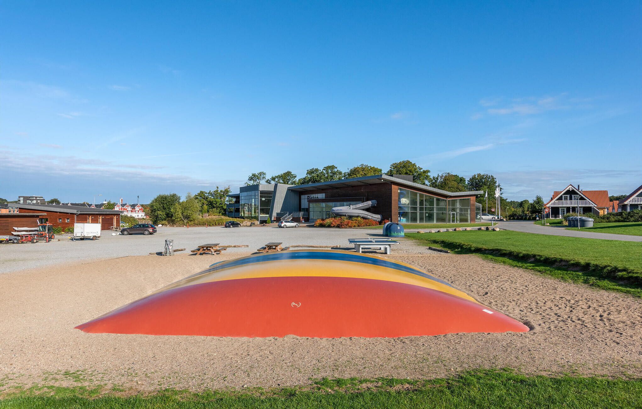 A modern building with a glass facade, a parking lot, and a colorful slide structure.