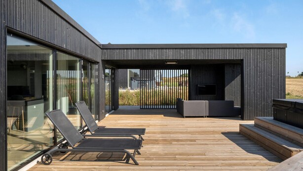 A modern outdoor deck with wooden flooring, a seating area with a sofa and chairs, and a large glass wall offering a view of the surrounding landscape. - Pet friendly home in Børkop with sauna (Børkop)