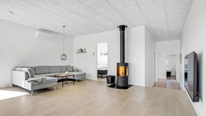 A modern living room with a grey sofa, a wooden coffee table, and a black wood-burning stove. - Pet friendly home in Børkop with sauna (Børkop)