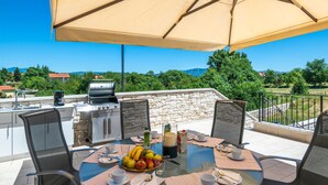 An outdoor patio with a grill, dining table, chairs, and a large umbrella. - Stunning home in Sumber (Sumber)