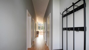 Un couloir doté d’un plancher en bois, de murs blancs et d’une étagère en métal noir pourvue de crochets.