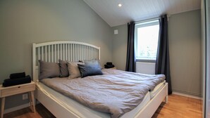 Une chambre à coucher avec un lit, des tables de chevet, une fenêtre et une vue sur la verdure.