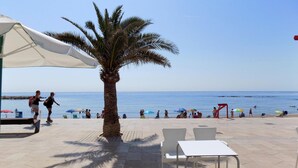 En terrasse ved stranden med palmetræ, hvidt bord og stole.