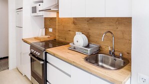 Et lille køkken med stålvask, indbygget ovn og opvaskestativ.
