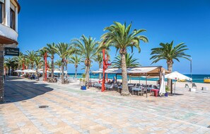Une promenade en bord de mer, bordée de palmiers, avec des espaces de repos en plein air et une vue sur la mer.