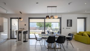 A modern kitchen with a dining area, large windows, and a yellow sofa. - Luxurious home in Grizane with sauna (Grizane)