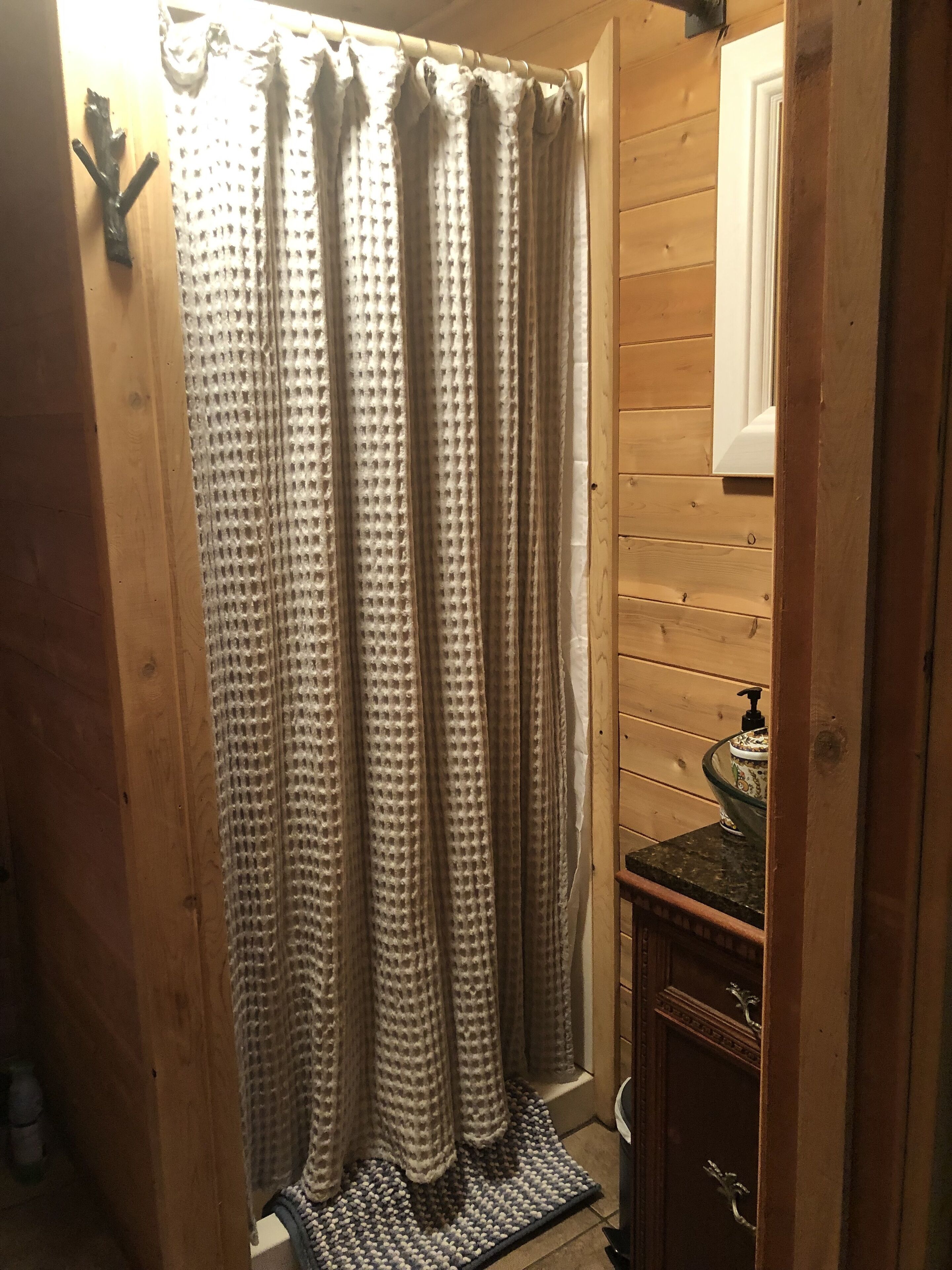 A bathroom with wooden walls, a shower curtain, a sink with a decorative bowl, and a small rug.