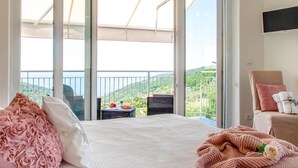 Une chambre d’hôtel avec un grand balcon, un lit avec une literie rose et blanche, et une chaise avec une couverture.