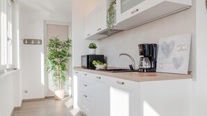 Une cuisine moderne avec des meubles blancs, un plan de travail en bois, un évier, une machine à café et une plante en pot.
