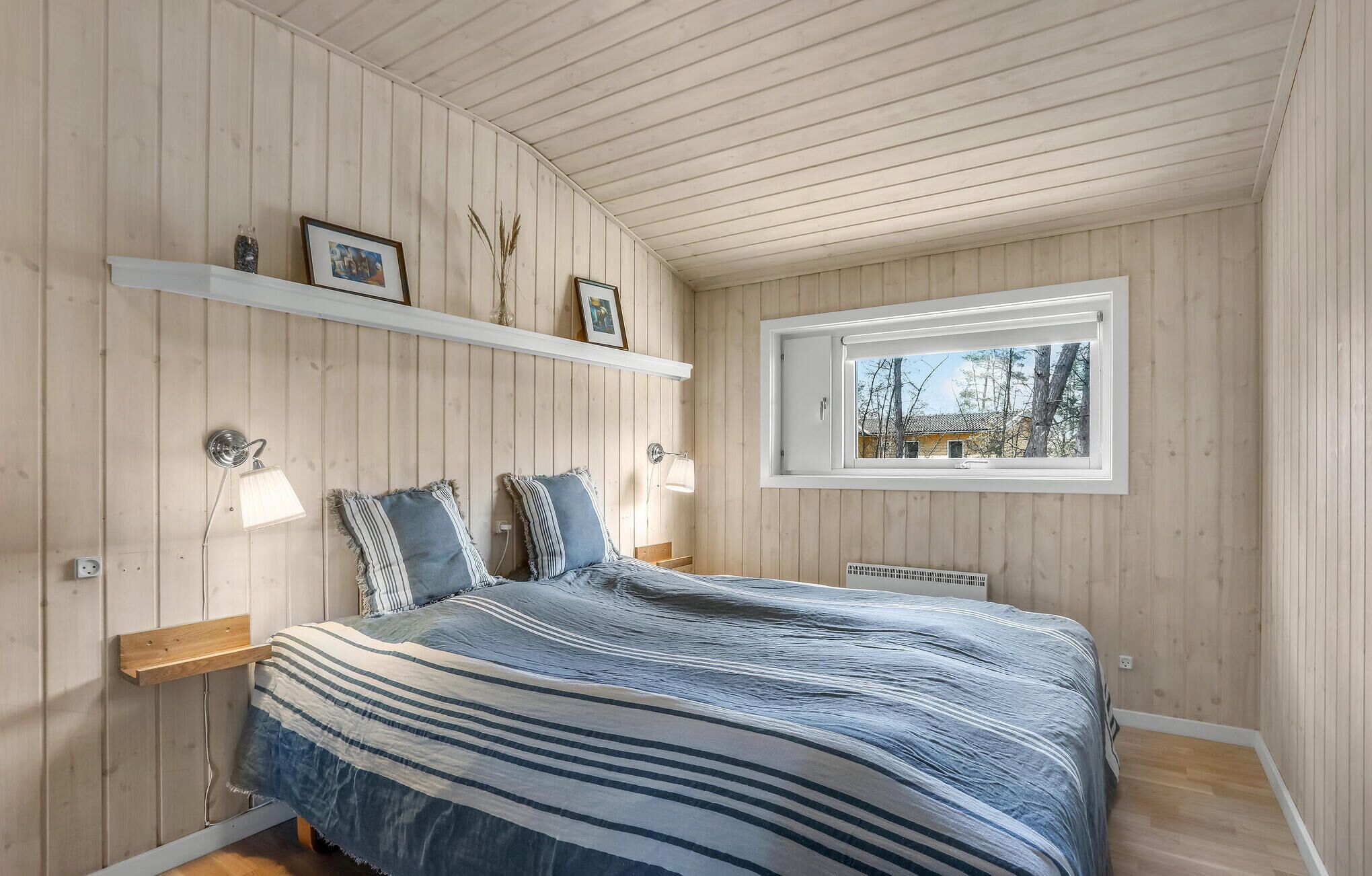 Un dormitorio con cama, paredes de madera, una ventana y una estantería con fotografías.