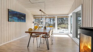 Et moderne spiseområde med et træbord, stole, et billede på væggen og et stort vindue med udsigt til træer.