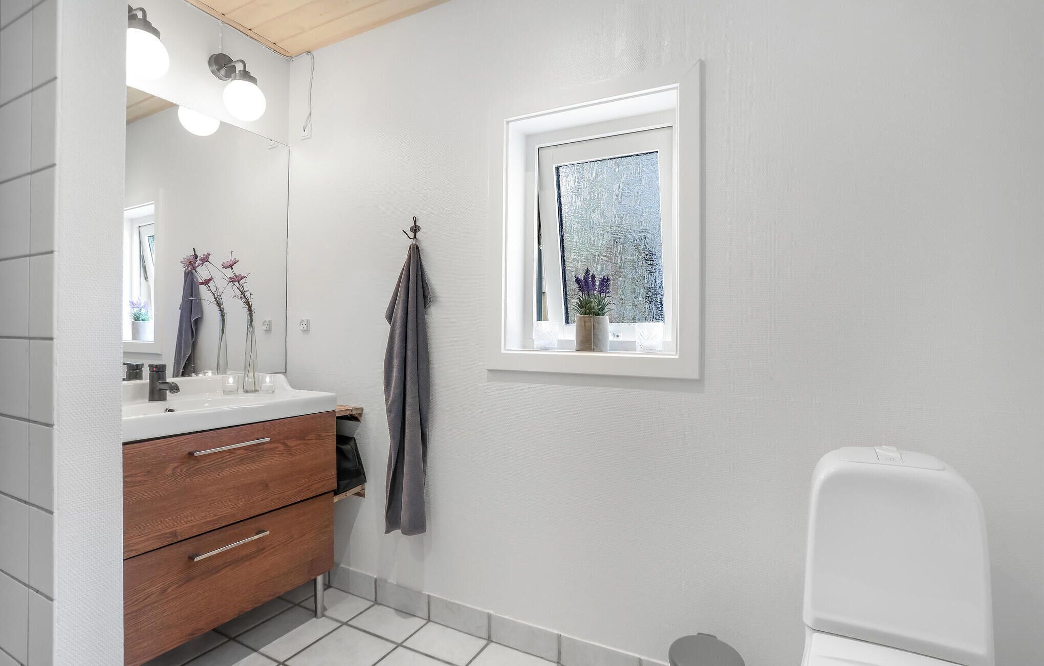 Een badkamer met een wit aanrichtmeubel, een spiegel, een raam met uitzicht en een toilet.
