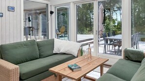 Et hyggeligt opholdsområde indendørs med en grøn sofa, et træbord og en fletstol.