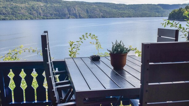 A wooden deck with a table and chairs overlooking a lake with forested hills in the background. - Lovely home in Vikersund with sauna (Vikersund)